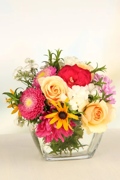Piękny bukiet kwiatów jasny w szklanym wazonie, na drewnianym stole, na jasnym tle — Zdjęcie stockowe