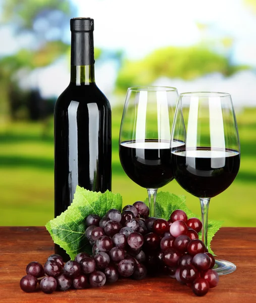 Ripe grapes, bottle and glasses of wine on bright background — Stok fotoğraf