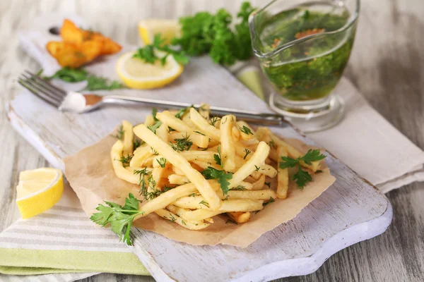 French fries on tracing paper on board on napkin wooden table — Stock Photo, Image