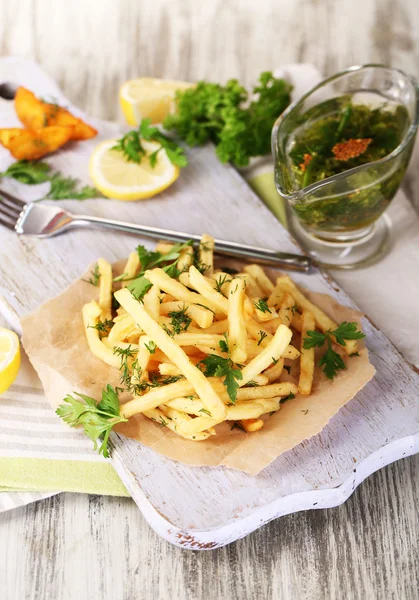 French fries on tracing paper on board on napkin wooden table — Stock Photo, Image