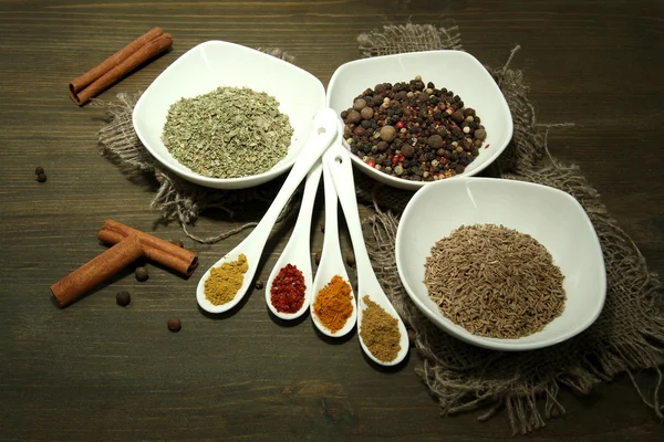 Surtido de especias en cucharas blancas y cuencos, sobre fondo de madera — Foto de Stock