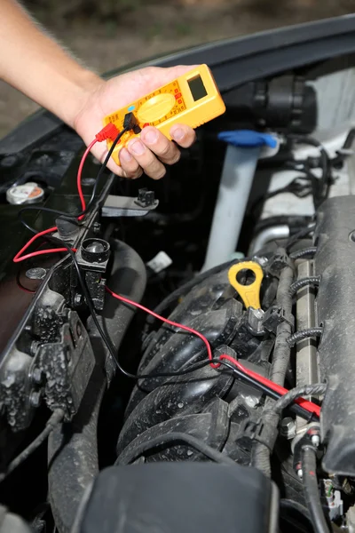 Mecánico automático utiliza voltímetro multímetro para comprobar el nivel de voltaje en la batería del coche — Foto de Stock