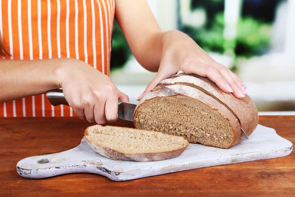 Cutting bread on wooden board on wooden table on window background — Stock Photo, Image