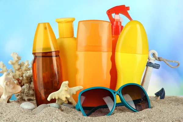 Flaschen mit Sonnencreme und Sonnenbrille, auf blauem Hintergrund — Stockfoto