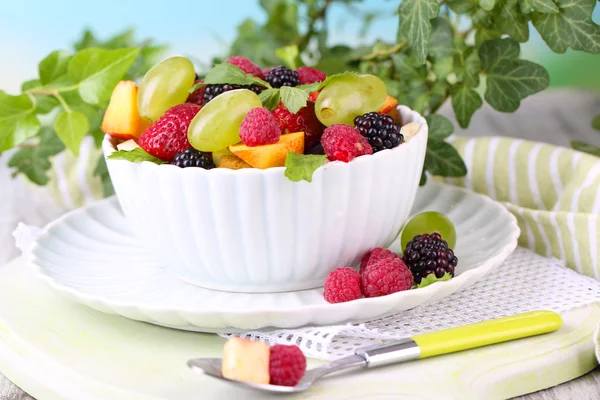 Fruit salad in bowl, on wooden table, on bright background Stock Picture