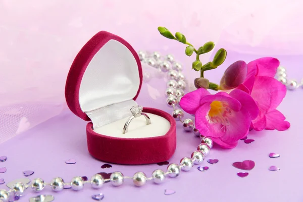 Caixa bonita com anel de casamento e flor no fundo roxo — Fotografia de Stock