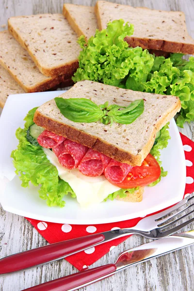 Lezzetli sandviç salam sosis ve ahşap masa arka plan üzerinde renkli peçete üzerinde sebze ve meyve suyu ile kompozisyon — Stok fotoğraf