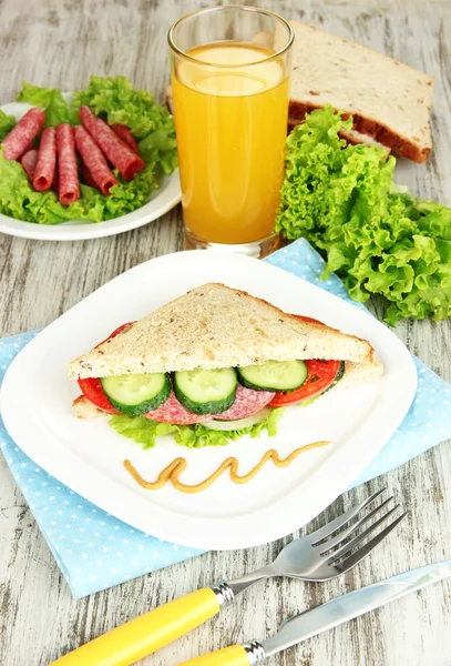 लाकडी टेबल पार्श्वभूमीवर सॅलामी सॉसेज आणि भाज्यांसह फळ रस आणि चवदार सँडविचसह रचना — स्टॉक फोटो, इमेज