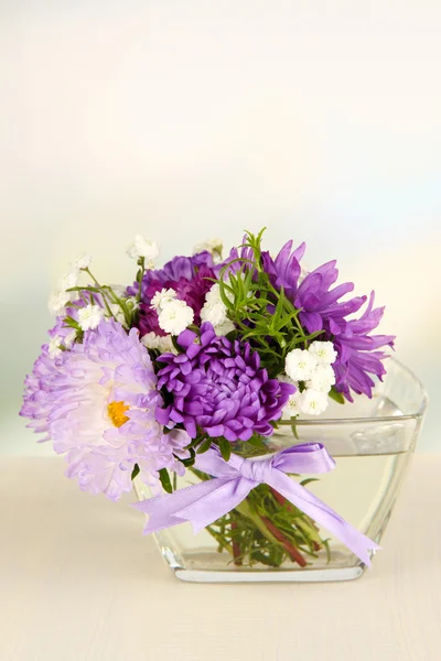 束美丽的鲜艳的花朵在玻璃花瓶，木桌上，在明亮的背景上 — 图库照片
