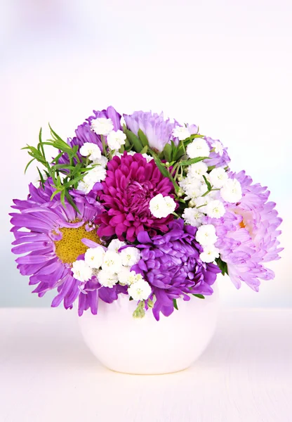 Hermoso ramo de flores brillantes en jarrón de color, sobre mesa de madera, sobre fondo brillante —  Fotos de Stock