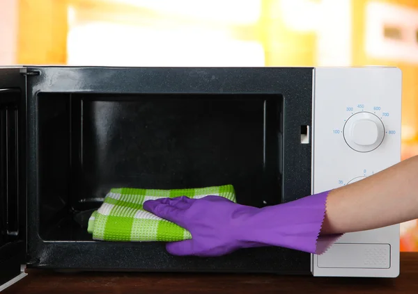 Χέρι με microfiber καθαρισμού φούρνο μικροκυμάτων, σε φωτεινό φόντο — Φωτογραφία Αρχείου