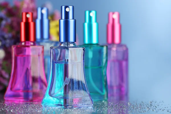 Perfume de mujer en hermosas botellas y flores sobre fondo azul — Foto de Stock