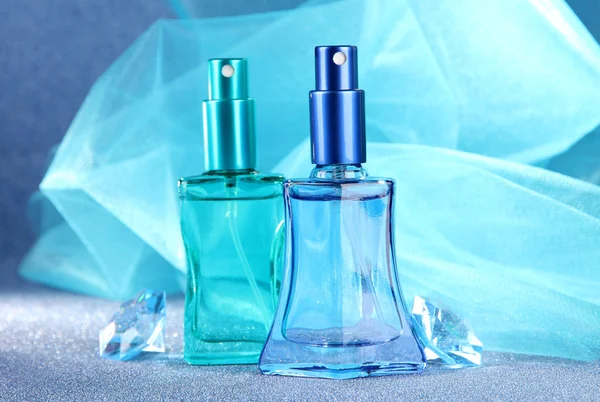 Perfume de mujer en hermosas botellas sobre fondo azul — Foto de Stock