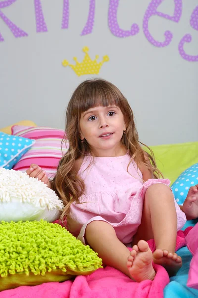 Menina sentada na cama no quarto no fundo da parede cinza — Fotografia de Stock