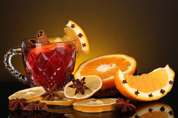 Duftender Glühwein im Glas mit Gewürzen und Orangen auf gelbem Hintergrund — Stockfoto