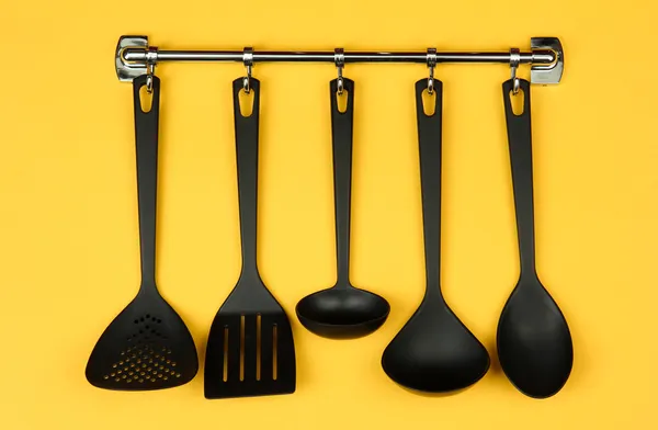 Utensílios de cozinha preto em ganchos de prata, no fundo amarelo — Fotografia de Stock