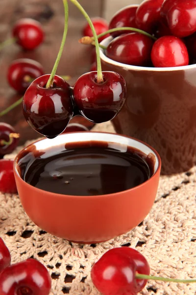 Reife rote Kirschbeeren in Tasse und Schokoladensauce auf Holztisch in Großaufnahme — Stockfoto