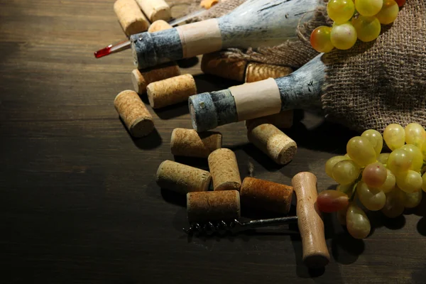 Old bottles of wine, grapes and corks on wooden background — Stock Photo, Image