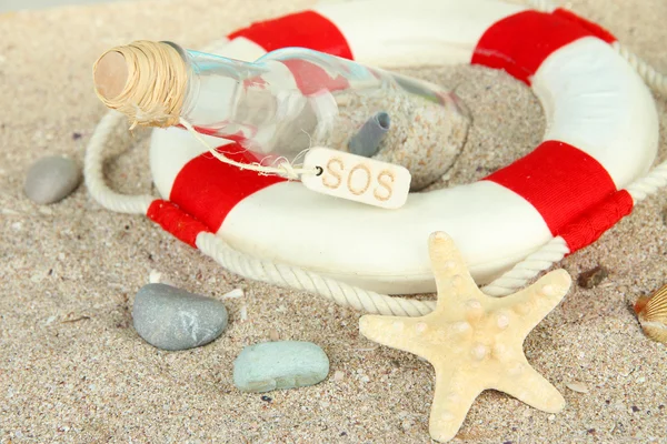 Glass of bottle with note inside on sand background — Stock Photo, Image