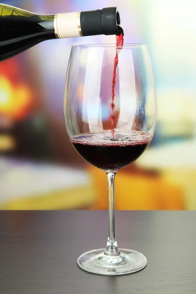 Vino tinto que se vierte en copa de vino, sobre fondo brillante — Foto de Stock