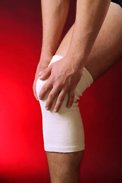Young man with elastic bandage on knee, on red background — Stock Photo, Image