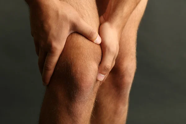 Молодой человек с болью в коленях на темном фоне — стоковое фото