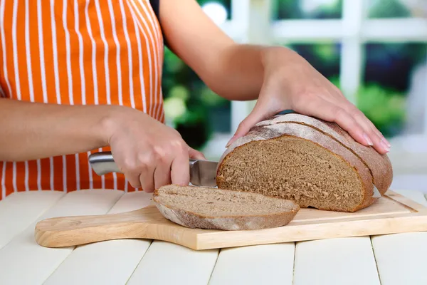 Cięcia chleba na desce na drewnianym stole na tle okna — Zdjęcie stockowe