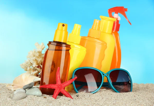 Botellas con crema bronceadora y gafas de sol, sobre fondo azul — Foto de Stock