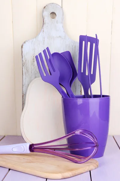 Utensílios de cozinha de plástico em copo na mesa de madeira — Fotografia de Stock