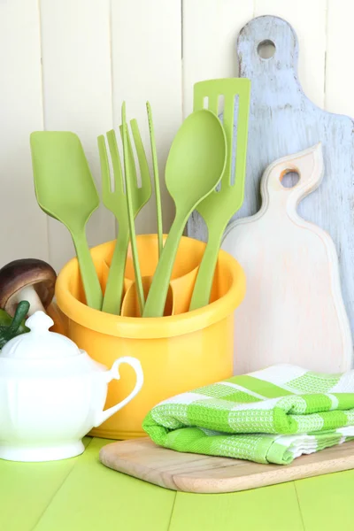 Plastic kitchen utensils in cup on wooden table — Stock Photo, Image