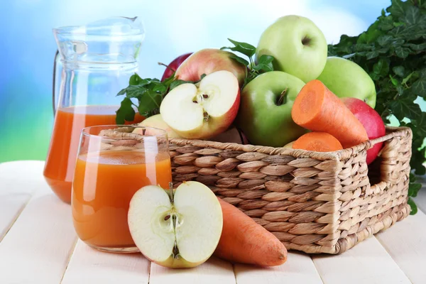 Sweet apples, juice and carrots on wooden table on natural background — Stock Photo, Image