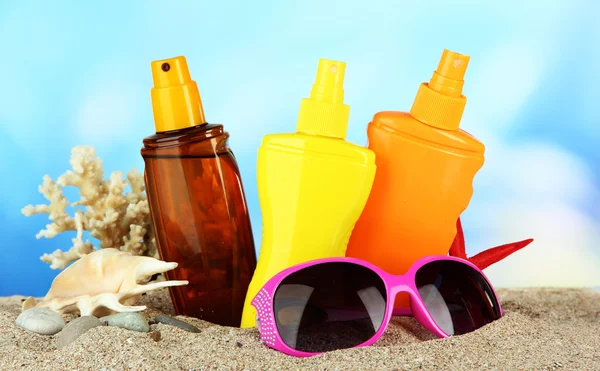 Bottles with suntan cream and sunglasses, on blue background — Stock Photo, Image