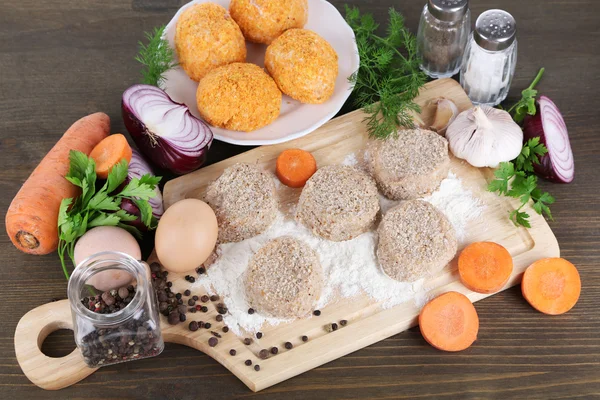 Meat patties on board and on plate on wooden table — Stock Photo, Image