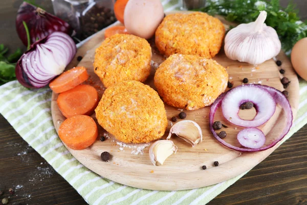 Meat patties on board on napkin on wooden table — Stock Photo, Image