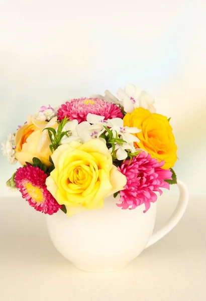 Beautiful bouquet of bright flowers in color mug, on wooden table, on light background — Stock Photo, Image