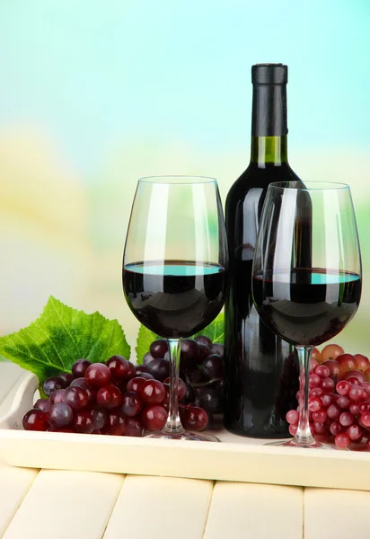 Ripe grapes, bottle and glasses of wine on tray, on bright background — Stock Photo, Image