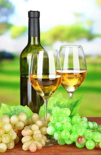 Ripe grapes, bottle and glasses of wine, on bright background — Stock Photo, Image