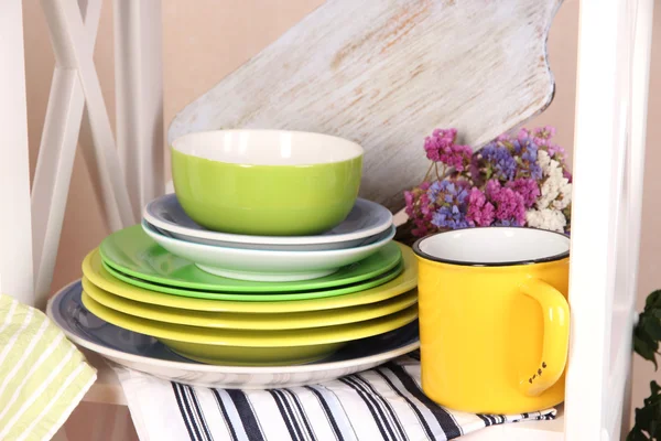 Beautiful white shelves with tableware and decor, on color wall background, close-up — Stock Photo, Image