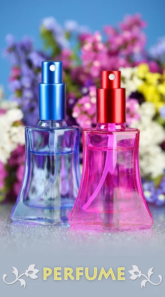 Frauenparfüm in schönen Flaschen und Blumen auf blauem Hintergrund — Stockfoto