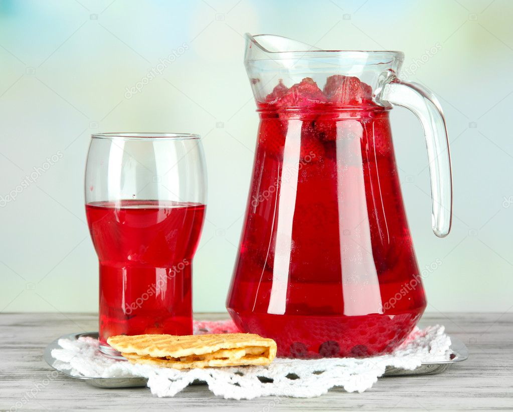 Pitcher and glass of compote on napkin on wooden table on light background