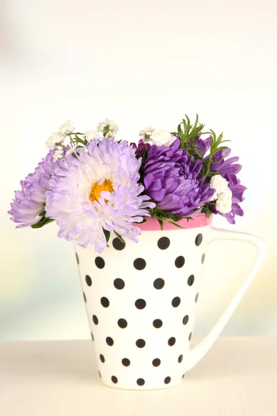 Beautiful bouquet of bright flowers in color mug, on wooden table, on light background — Stock Photo, Image