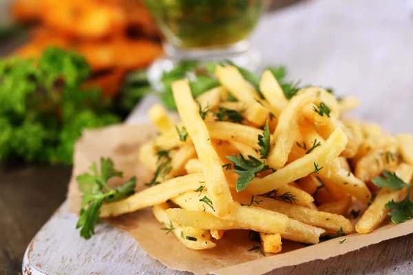 French fries on tracing paper on board on wooden table — Stock Photo, Image