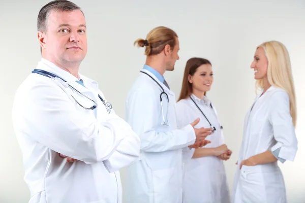 Médecin debout devant ses collègues sur fond gris — Photo