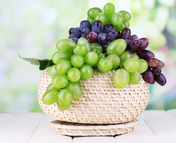 Uvas verdes e roxas maduras em cesta sobre mesa de madeira sobre fundo natural — Fotografia de Stock