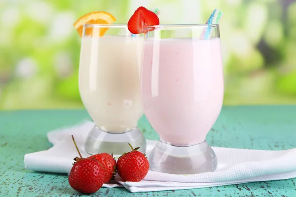 Leckere Milchshakes mit Orangen und Erdbeeren auf Holztisch vor natürlichem Hintergrund — Stockfoto