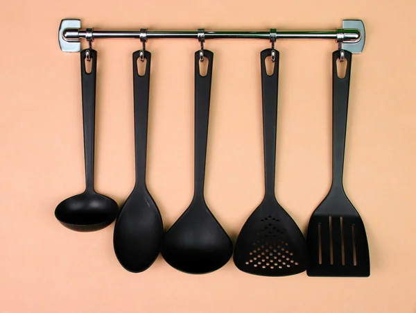 Ustensile de bucătărie neagră pe cârlige de argint, pe fundal piersici — Fotografie, imagine de stoc