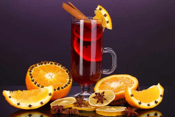 Fragrant mulled wine in glass with spices and oranges around on purple background — Stock Photo, Image