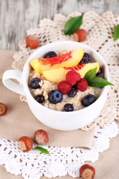 Oatmeal in cup with berries on napkins on wooden table — Stock Photo, Image