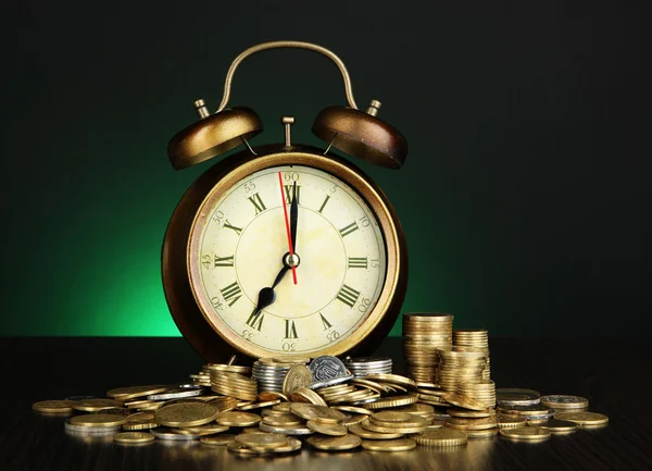 Horloge antique et pièces de monnaie sur table en bois sur fond de couleur sombre — Photo