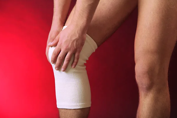 Junger Mann mit elastischem Verband am Knie, auf rotem Hintergrund — Stockfoto